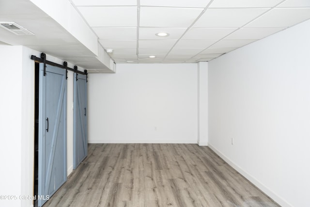 below grade area with a barn door, light wood-style flooring, recessed lighting, a paneled ceiling, and baseboards