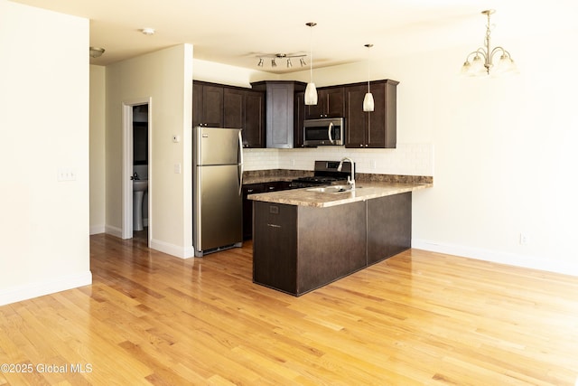 kitchen with appliances with stainless steel finishes, a peninsula, dark brown cabinetry, decorative backsplash, and light wood-style flooring