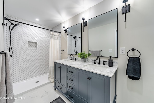 bathroom with marble finish floor, a tile shower, double vanity, and a sink