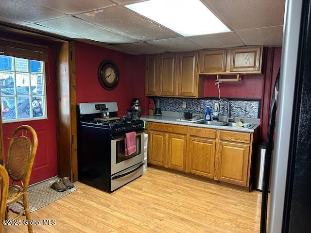kitchen featuring a sink, light wood-type flooring, light countertops, appliances with stainless steel finishes, and a paneled ceiling