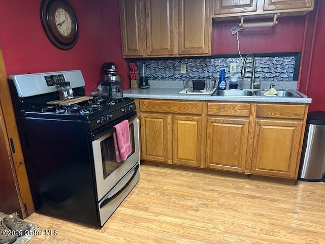 kitchen featuring stainless steel range with gas cooktop, tasteful backsplash, a sink, brown cabinets, and light countertops