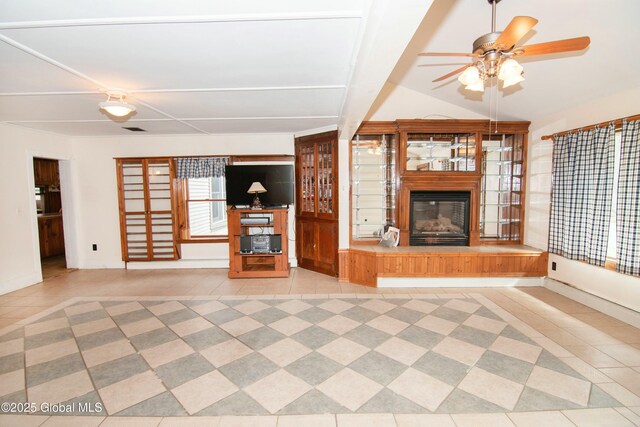 unfurnished living room featuring baseboards, a ceiling fan, a glass covered fireplace, and tile patterned flooring