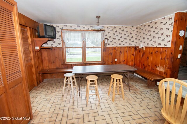 dining room featuring wooden walls, a wainscoted wall, brick patterned floor, and wallpapered walls