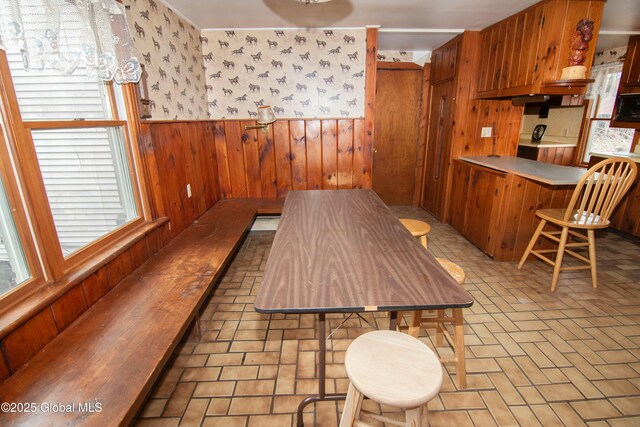 dining space with wooden walls, wainscoting, brick floor, and plenty of natural light
