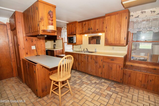 kitchen with brown cabinetry, light countertops, a peninsula, and brick patterned floor