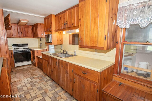 kitchen featuring a sink, white range with gas cooktop, stainless steel microwave, and light countertops