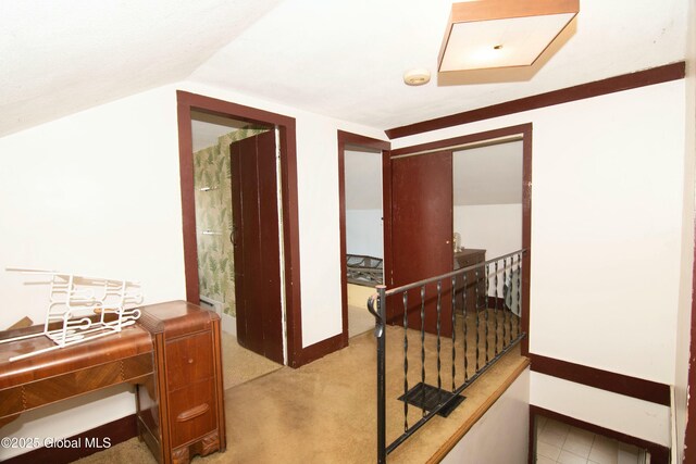 hallway featuring baseboards, an upstairs landing, vaulted ceiling, and light carpet