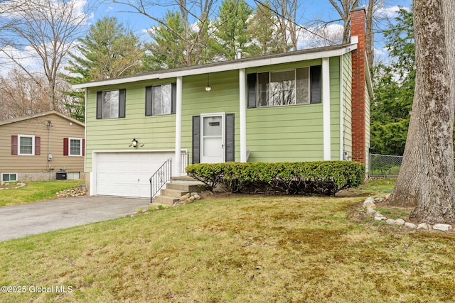 split foyer home featuring driveway, a chimney, a front yard, a garage, and fence