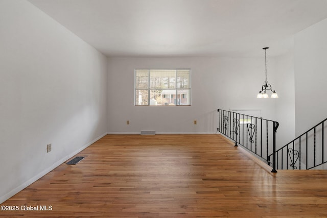 empty room with baseboards, a chandelier, wood finished floors, and visible vents
