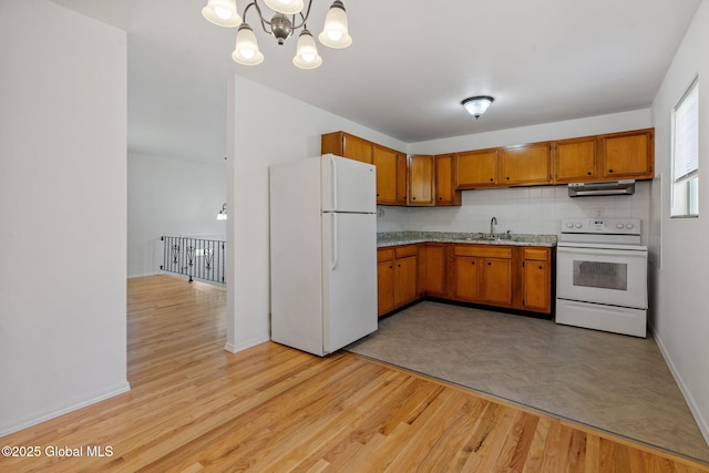 kitchen with brown cabinets, a sink, a chandelier, light wood-style floors, and white appliances