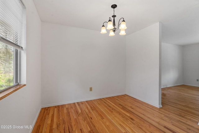 spare room with baseboards, light wood-style flooring, and a notable chandelier