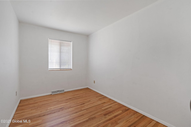 empty room with baseboards, visible vents, and light wood-type flooring