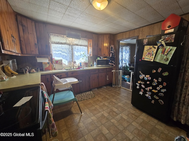 kitchen featuring brick patterned floor, wood walls, light countertops, a sink, and black appliances