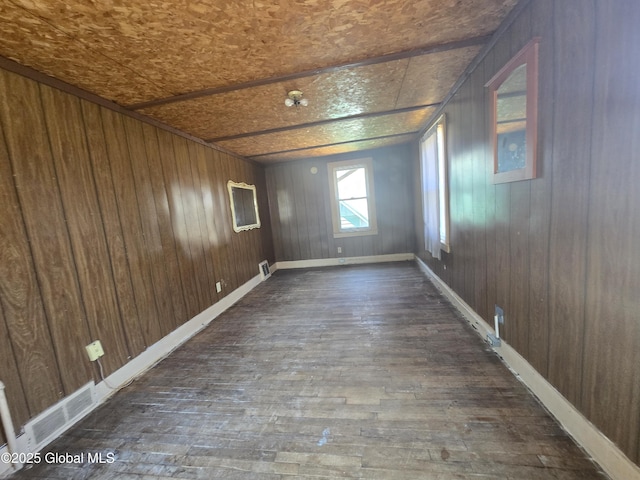 unfurnished room featuring dark wood finished floors, baseboards, wooden walls, and visible vents