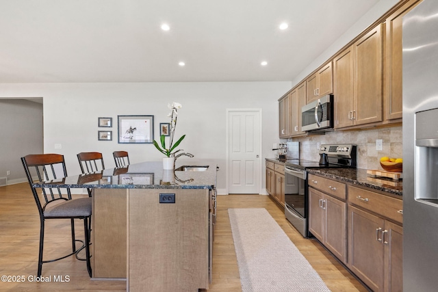 6 Gorsline Dr, Halfmoon, NY 12118 - kitchen with stainless steel appliances, a kitchen island with sink, dark stone countertops, light wood-style floors, and a breakfast bar area