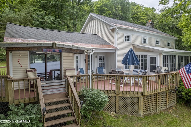 rear view of property with a wooden deck, a sunroom, and a shingled roof