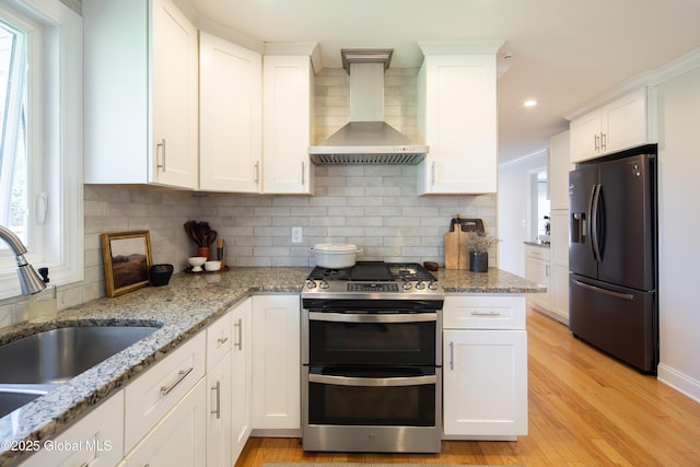 kitchen featuring wall chimney exhaust hood, a sink, double oven range, plenty of natural light, and refrigerator with ice dispenser