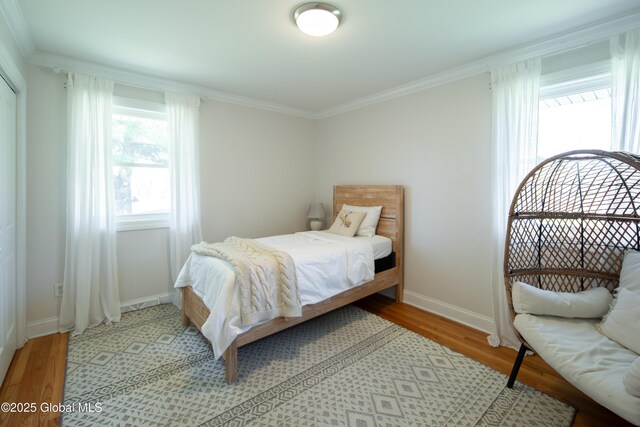 bedroom with baseboards, crown molding, and light wood finished floors