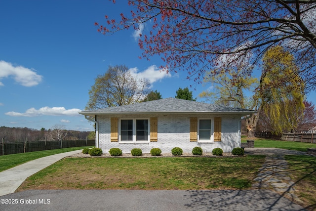 view of front of home featuring brick siding, roof with shingles, a front yard, and fence