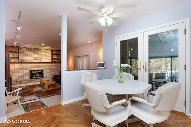 dining area with a ceiling fan, french doors, a fireplace, track lighting, and baseboards