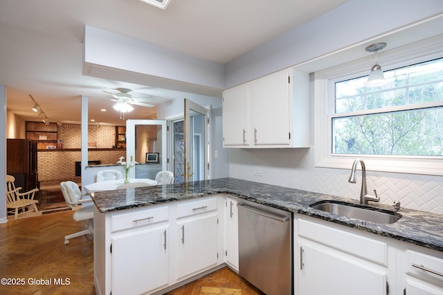 kitchen with white cabinets, a sink, brick wall, a peninsula, and stainless steel dishwasher