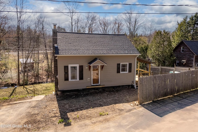bungalow with roof with shingles, a chimney, and fence