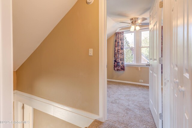 corridor featuring lofted ceiling, baseboards, and light colored carpet