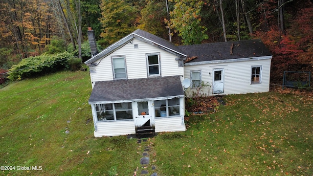 split level home with a chimney, roof with shingles, a sunroom, a forest view, and a front yard