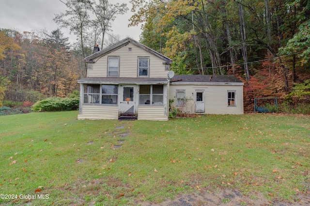 back of house featuring a lawn, a chimney, a view of trees, roof with shingles, and a sunroom