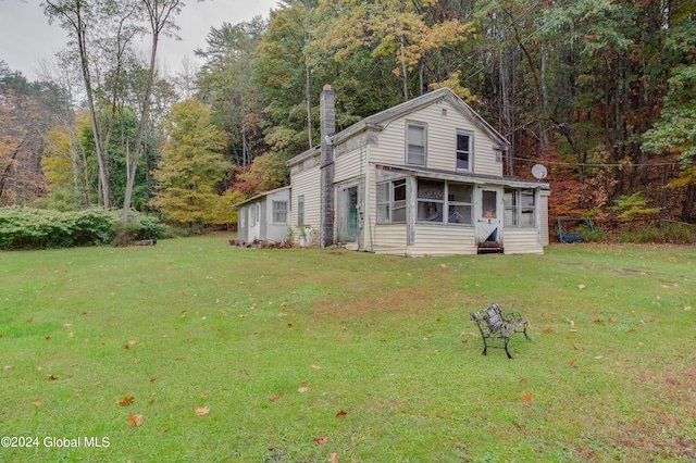 view of front facade featuring a wooded view, a sunroom, a chimney, and a front lawn