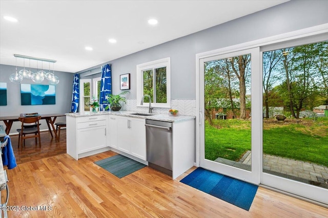 kitchen featuring dishwasher, a sink, white cabinets, tasteful backsplash, and light stone counters