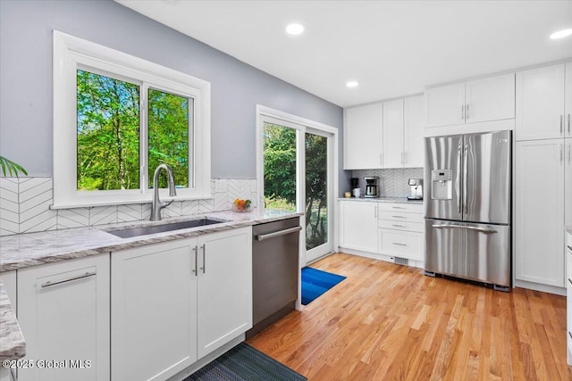 kitchen with appliances with stainless steel finishes, a sink, tasteful backsplash, white cabinetry, and light wood-style floors