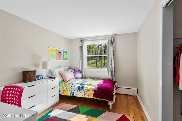 bedroom featuring a baseboard heating unit, wood finished floors, and baseboards