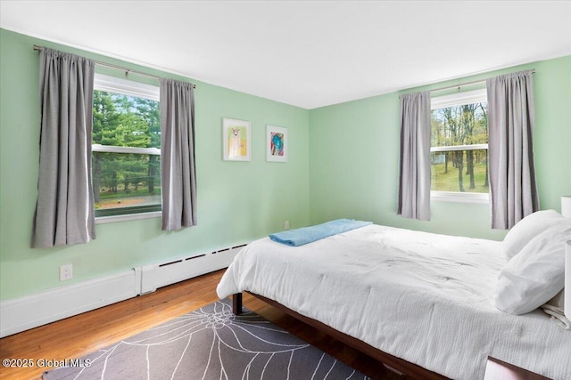 bedroom with multiple windows, wood finished floors, and a baseboard radiator