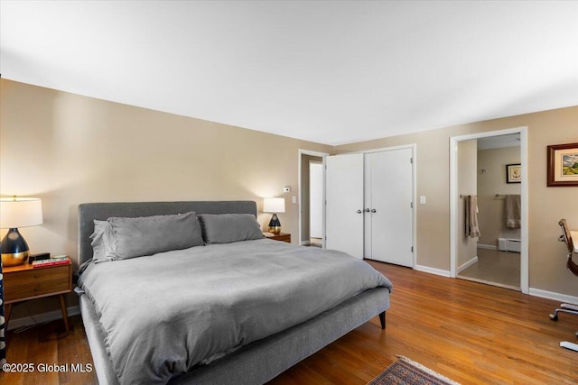 bedroom with baseboard heating, wood finished floors, baseboards, and ensuite bathroom