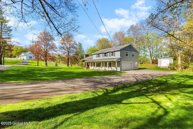 view of front of property with an attached garage, covered porch, driveway, a shed, and a front yard