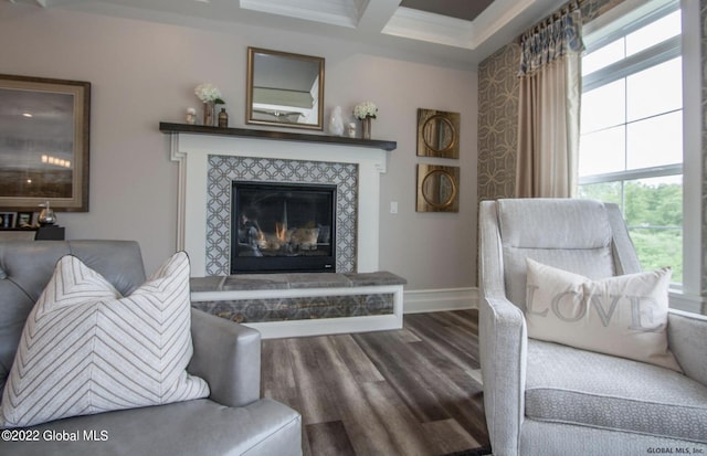 living area with beam ceiling, a tiled fireplace, baseboards, wood finished floors, and crown molding