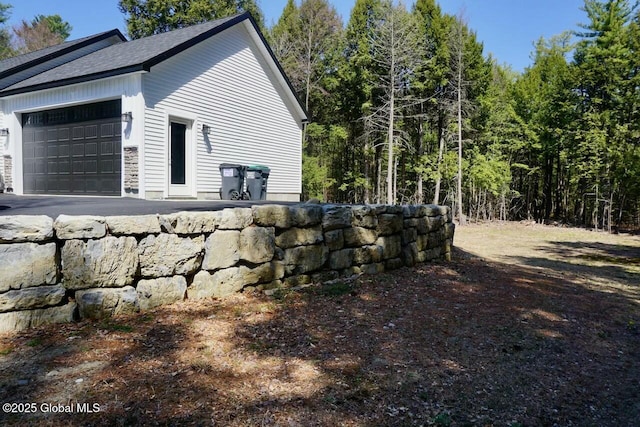 view of side of property featuring an attached garage, roof with shingles, and a wooded view