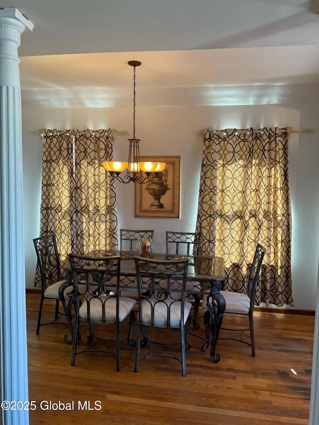 dining room with a notable chandelier, wood finished floors, and ornate columns