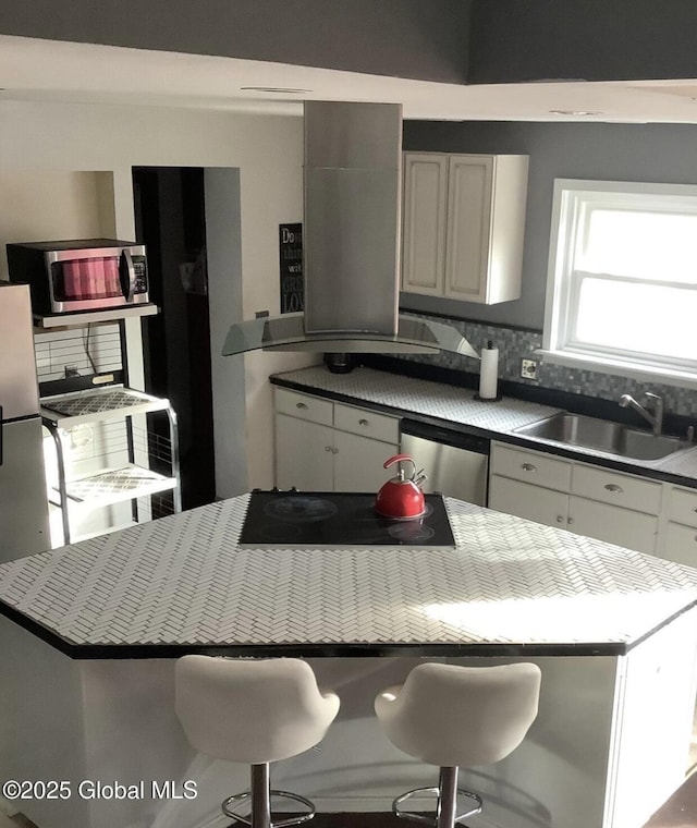 kitchen featuring stainless steel appliances, backsplash, a sink, white cabinetry, and a center island