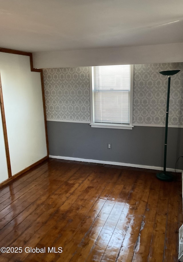 spare room featuring baseboards, wallpapered walls, wainscoting, and wood-type flooring