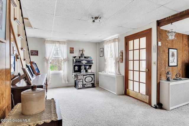 interior space featuring carpet flooring, wood walls, and a paneled ceiling