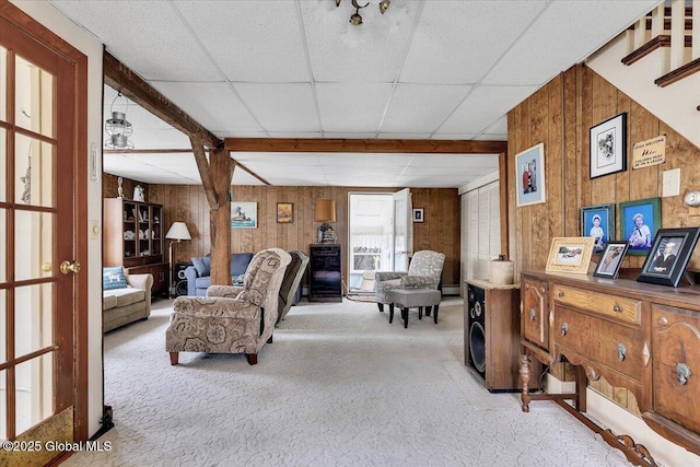 carpeted living room featuring wood walls and a drop ceiling
