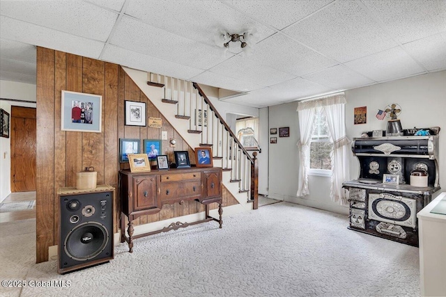 interior space with baseboards, wood walls, a paneled ceiling, and carpet