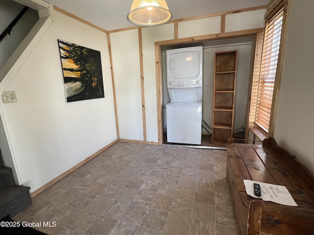 washroom featuring baseboards, stacked washer / drying machine, and laundry area