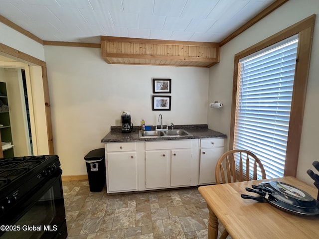 kitchen featuring dark countertops, black gas stove, white cabinetry, and a sink