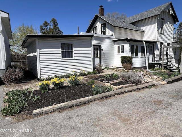 traditional-style home with a chimney, fence, and roof with shingles