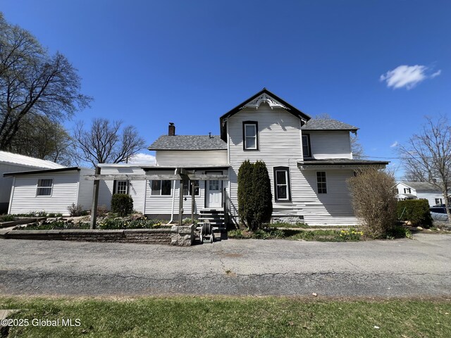 view of front of house with a shingled roof, a chimney, and entry steps