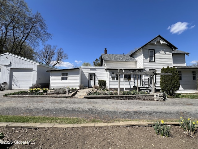 traditional home featuring a pergola, a detached garage, a chimney, a shingled roof, and an outdoor structure