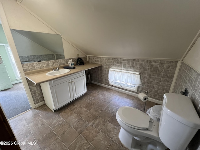 bathroom featuring vaulted ceiling, vanity, toilet, and tile walls